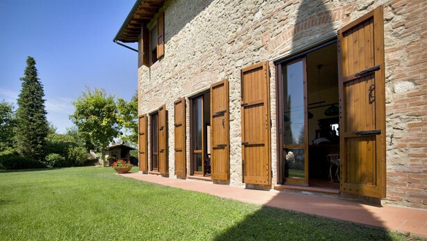 A stone building with wooden shutters and a well-maintained lawn.