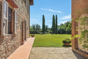 A narrow courtyard with a paved walkway, a grassy lawn, and tall cypress trees.
