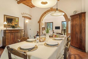 Een eethoek met een lange tafel gedekt voor een maaltijd, houten stoelen, een kroonluchter en een rustieke bakstenen boog.
