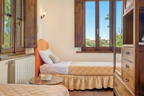 Een slaapkamer met twee bedden, een houten dressoir, een kleine tafel en een raam met uitzicht op groen.