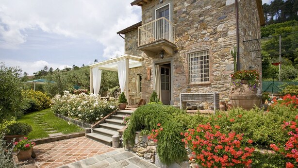 Ein Steinhaus mit Balkon, einem Blumen-Garten und einer Pergola.