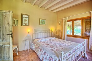 Ein Schlafzimmer mit Bett, Nachttisch, Fenster mit Vorhängen und Wandbildern.