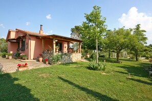 Ein Haus mit Stein Fundament, einem Ziegeldach und einem Garten mit verschiedenen Pflanzen und einer Rasenfläche.