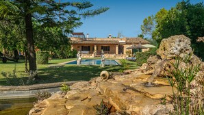 A stone pool with a fountain, surrounded by rocks and plants, in front of a house with a tiled roof and a patio area. - CA SA NINA - Villa with private pool in Inca. Free WiFi (Inca)