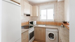 A compact kitchen with a microwave, sink, oven, and washing machine. - LLAMÀNTOL - Cosy house with private terrace near the beach. (Oliva)
