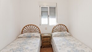 A small bedroom with two single beds, a window with blinds, and a bedside table with a lamp. - LLAMÀNTOL - Cosy house with private terrace near the beach. (Oliva)