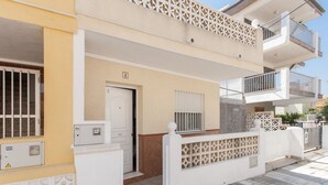 A two-story residential building with a white exterior, a balcony on the upper floor, and a gated entrance. - LLAMÀNTOL - Cosy house with private terrace near the beach. (Oliva)