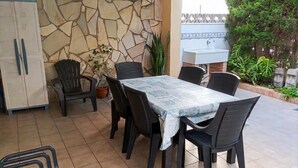 A patio with a stone wall, a table with chairs, a potted plant, and a sink. - LLAMÀNTOL - Cosy house with private terrace near the beach. (Oliva)