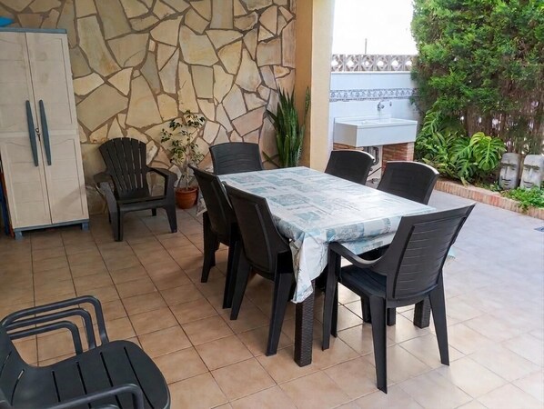 Une terrasse avec un mur en pierre, une table avec des chaises, une plante en pot et un évier.