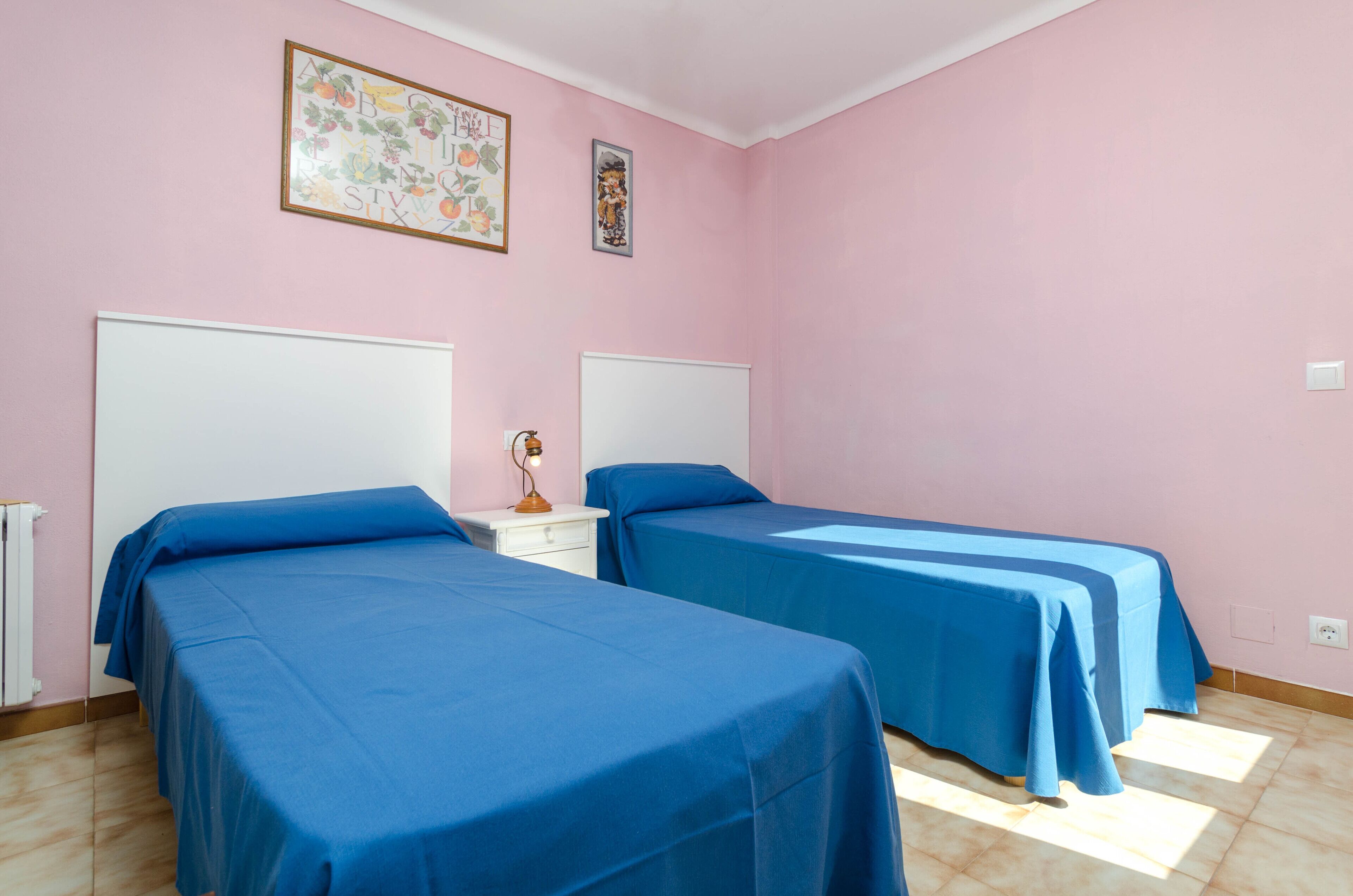 Ein Zimmer mit zwei Einzelbetten, einem weißen Nachttisch und einem kleinen Tisch mit einer Lampe.