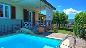 Ein Swimmingpool mit einer Steindeck, eine überdachte Terrasse mit Gartenmöbeln und ein Blick auf die Berge im Hintergrund.