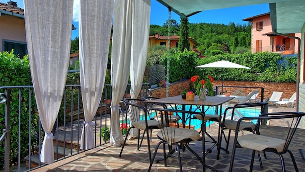 Ein überdachter Außenbereich mit Tischen, Stühlen, einem Pool und Blick auf Häuser und Grünflächen.