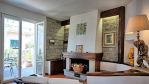 Ein gemütliches Wohnzimmer mit Kamin aus Stein, einer Bank und Blick auf die Terrasse.