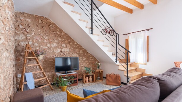 Ein gemütliches Wohnzimmer mit Steinwand, einer Holztreppe, einem Fernseher und einem Sofa.