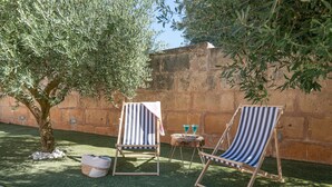 Zwei gestreifte Loungesessel, ein kleiner Tisch mit Getränken und ein Baum in einem Innenhof mit einer Steinmauer.