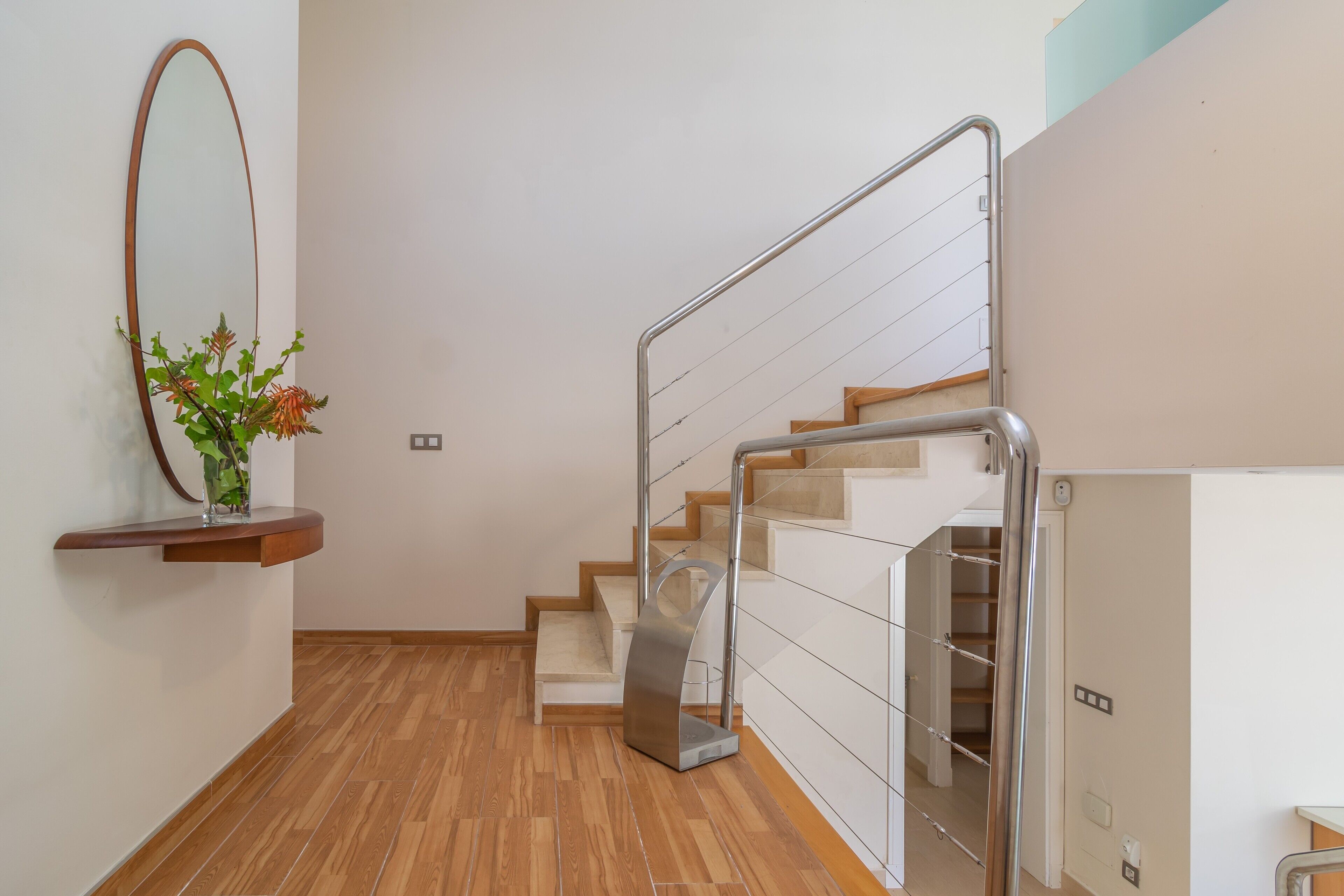 A modern staircase with a metal railing, wooden steps, and a wall-mounted mirror.