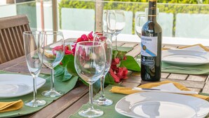 Mesa de jantar posta com copos de vinho, pratos e uma garrafa de vinho, com vista para o verde ao fundo.