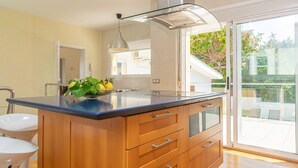 Uma cozinha moderna com uma ilha grande, armários de madeira e uma porta de correr envidraçada que dá para uma varanda.