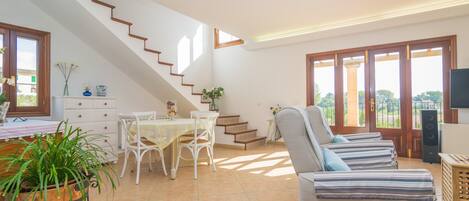 Un grand espace de vie comprenant un escalier, une table à manger avec des chaises, un canapé et un téléviseur.