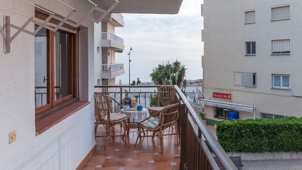 Un balcón con mobiliario de mimbre, una mesa y vista al mar.