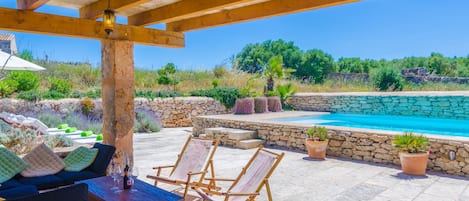 A covered outdoor area with a pool, stone walls, and seating.
