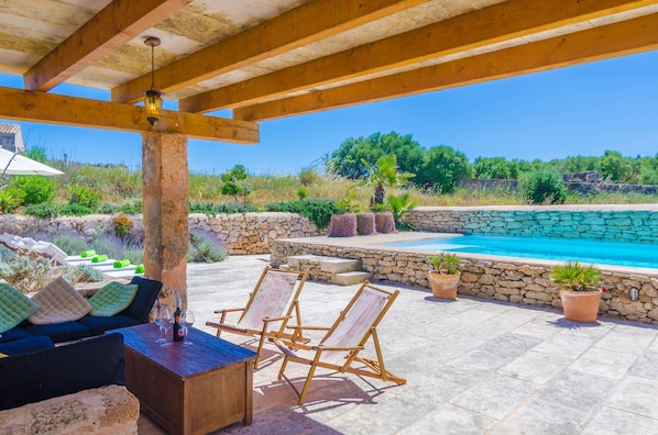 A covered outdoor area with a pool, stone walls, and seating.