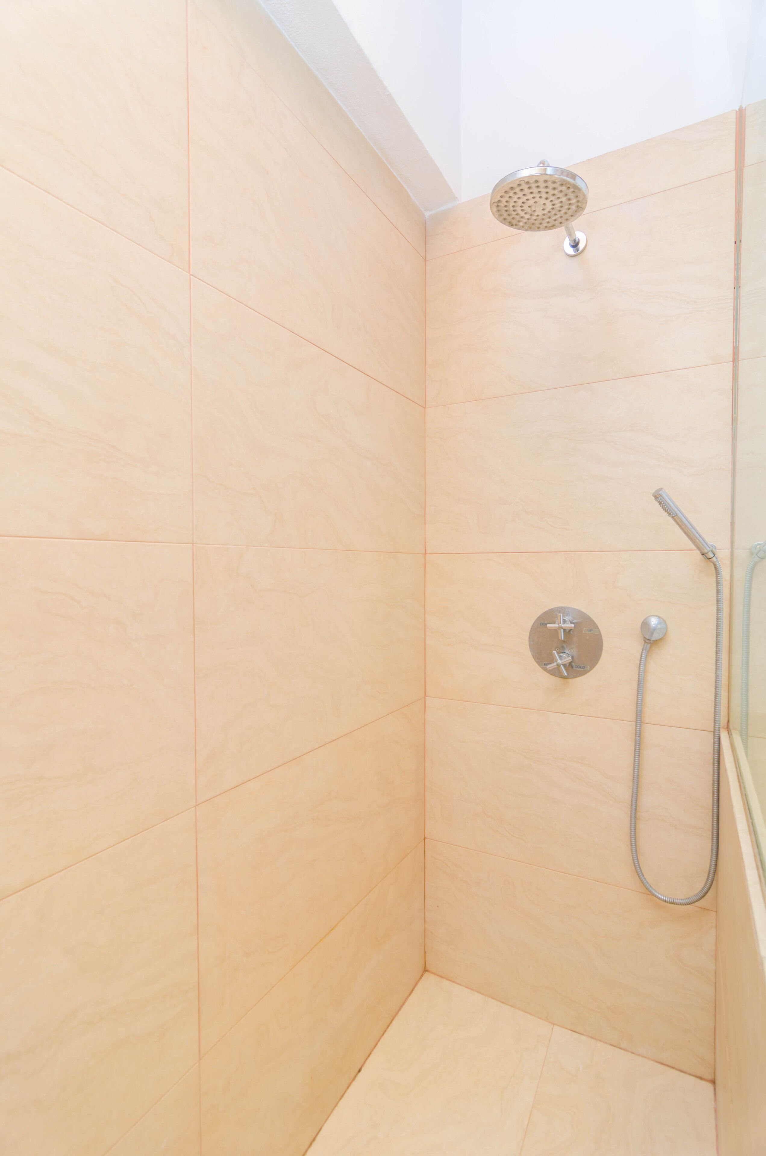 A shower with a handheld showerhead and a wall-mounted faucet.