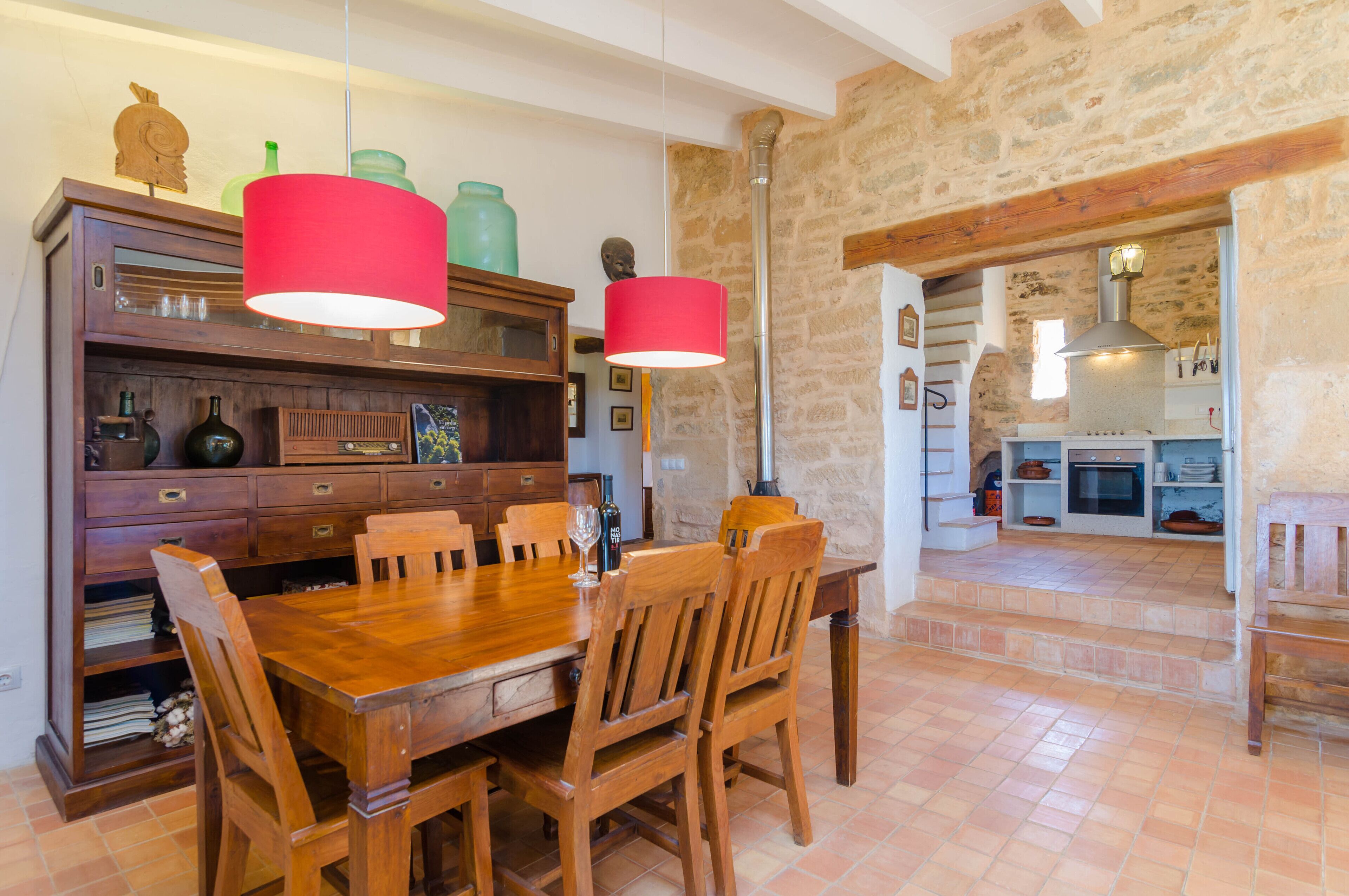 Un comedor con mesa y sillas de madera, una lámpara colgante roja y una pared de piedra.