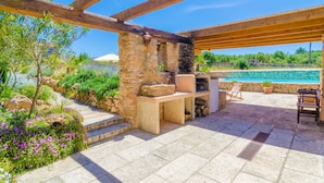Un patio al aire libre con suelo de piedra, pérgola de madera, paredes de piedra y vista al mar.