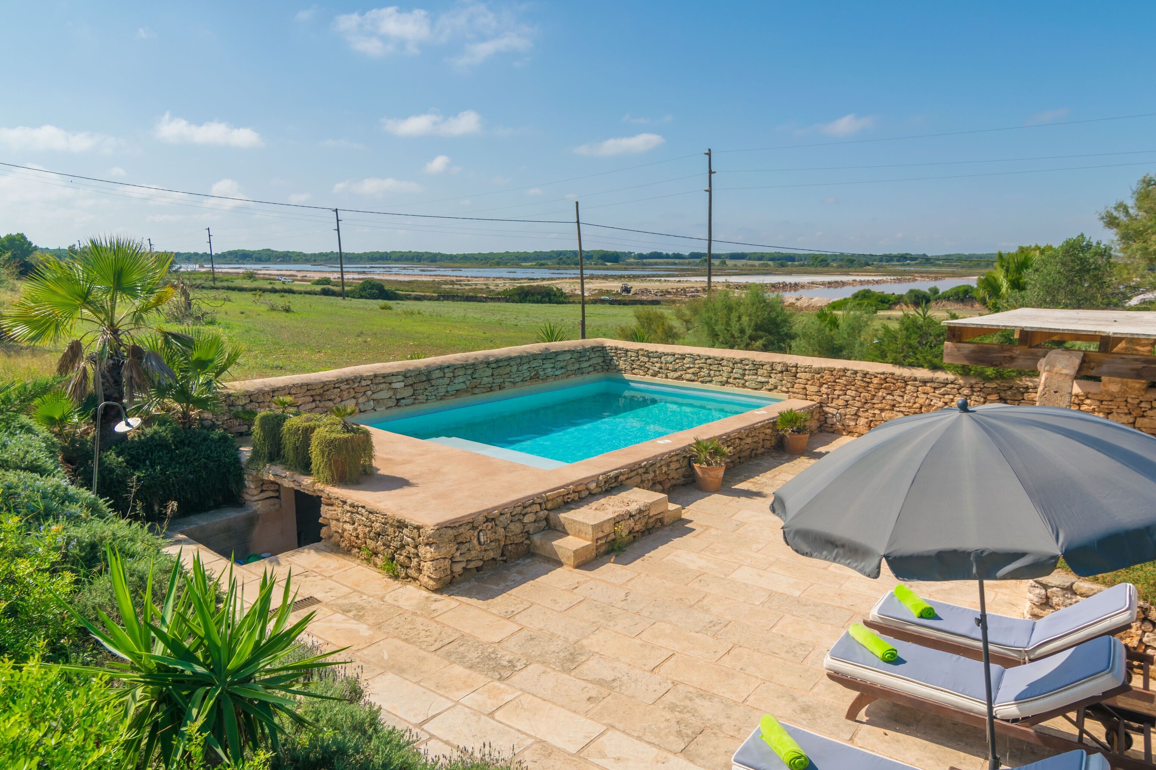 A stone pool surrounded by greenery, with lounge chairs and an umbrella.