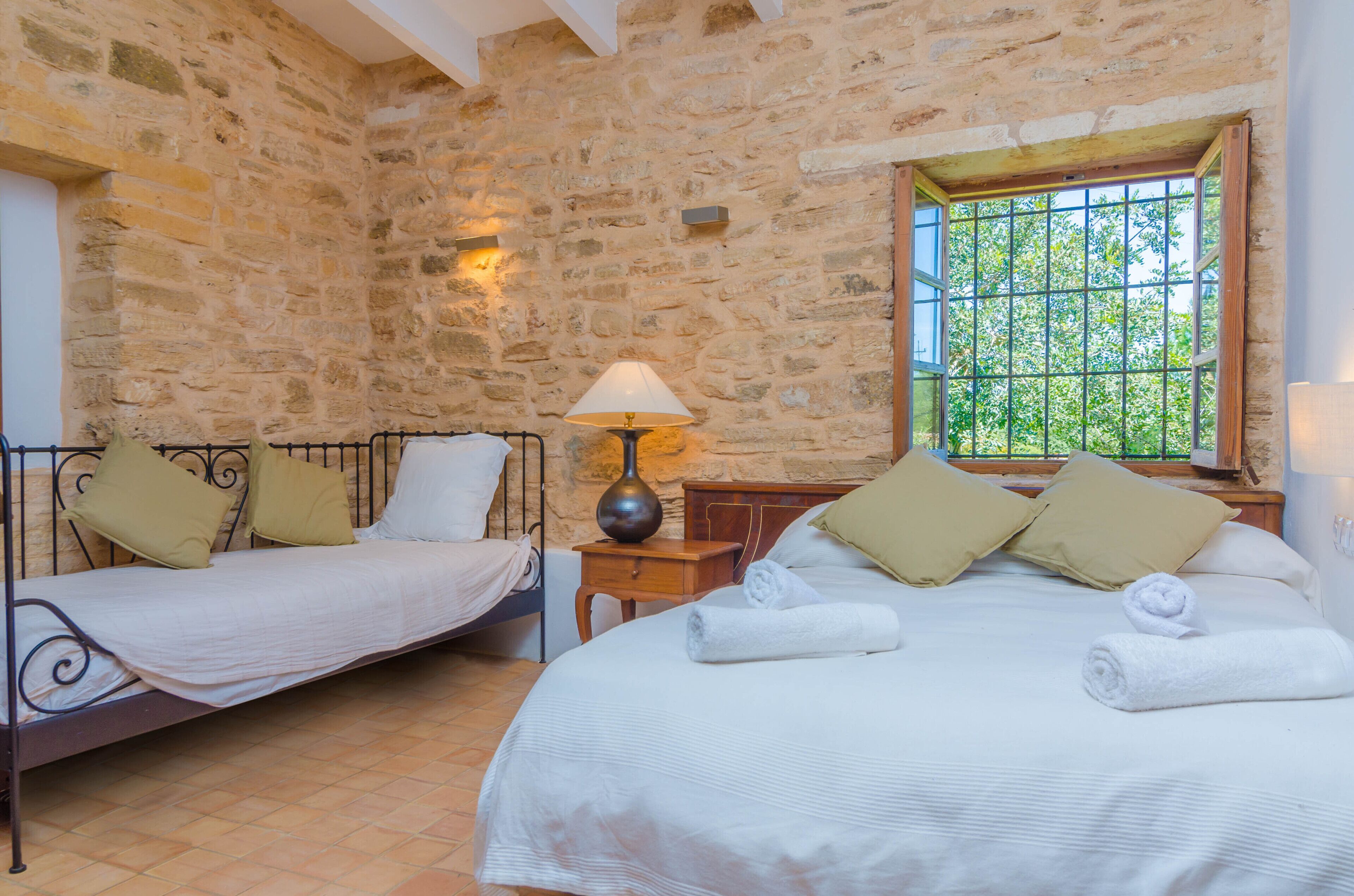 Una habitación con dos camas, paredes de piedra, una ventana con vistas y una lámpara en la mesita de noche.