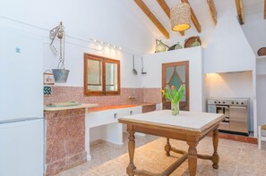 A kitchen with a marble countertop, wooden table, hanging light fixture, and stainless steel oven.