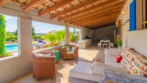 A covered outdoor lounge area with wicker furniture, a pool, and a view of greenery. - TORRE MARINA - Villa with private pool in Sa Ràpita. Free WiFi (Sa Ràpita)