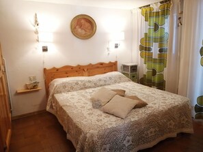 A bedroom with a wooden headboard, a bed with a floral bedspread, two bedside lamps, a small bedside table, and a wall-mounted picture. - Cosy apartment for 3 people with WIFI and TV (Marina Di Castagneto Carducci)
