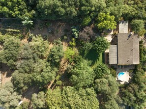 Vista aérea de uma propriedade com piscina, cercada por vegetação densa e estrutura de telhado em azulejos.