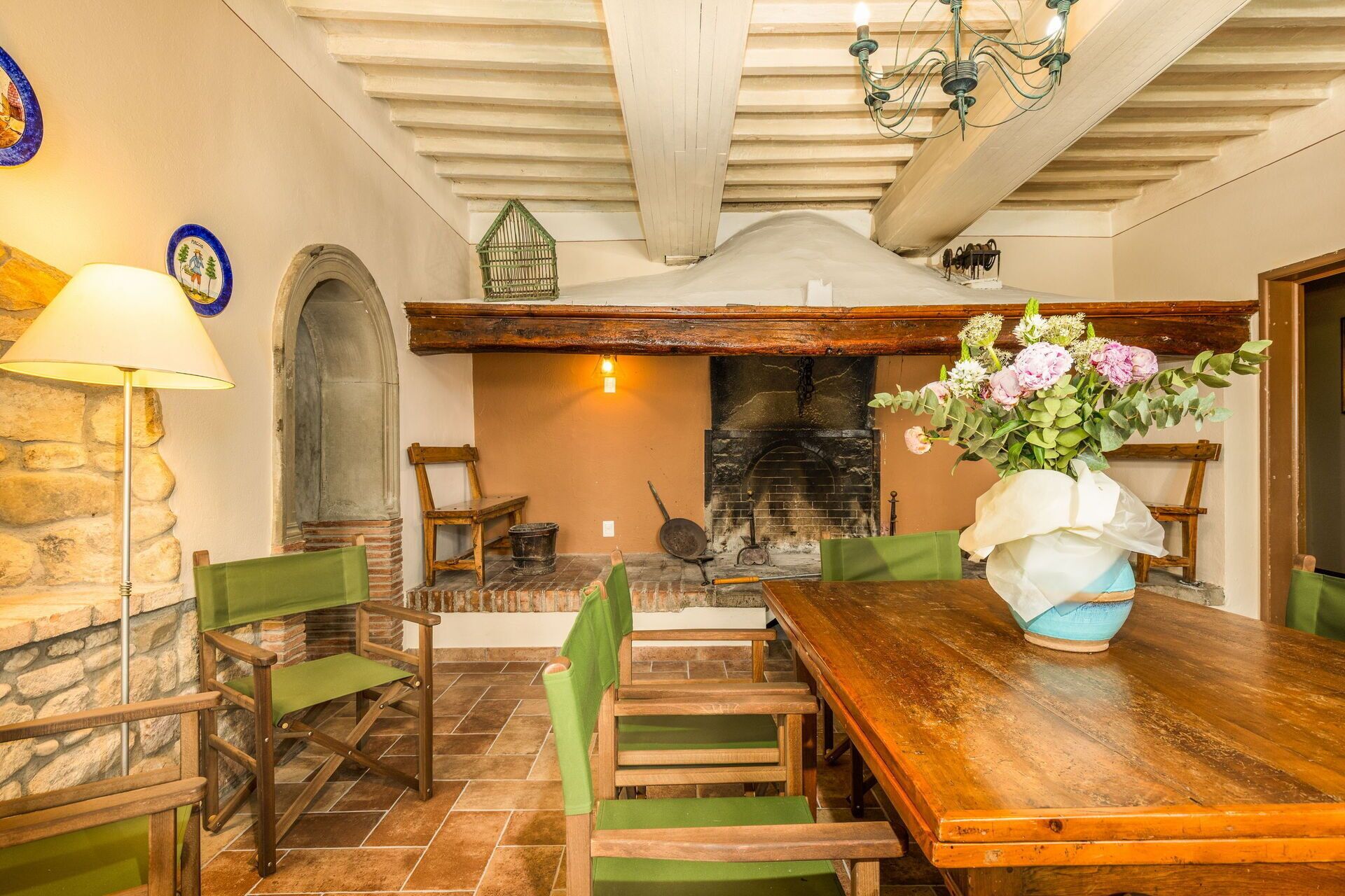 A rustic dining area with a wooden table, green chairs, a stone wall, and a fireplace.
