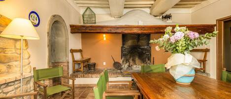 A rustic dining area with a wooden table, green chairs, a stone wall, and a fireplace.