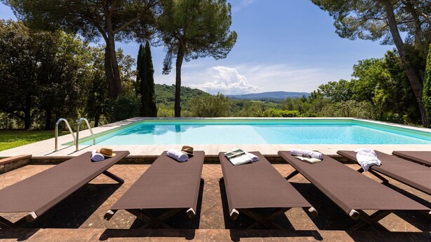 Una piscina con sillas de descanso y vistas a un paisaje boscoso.