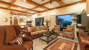 A spacious living room with a high ceiling, wooden beams, a large window with a view, and a cozy seating area with a sofa and chairs.