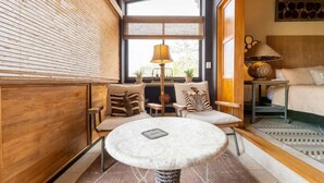 A cozy room with a round table, two sofas, a bed, and a window with blinds.