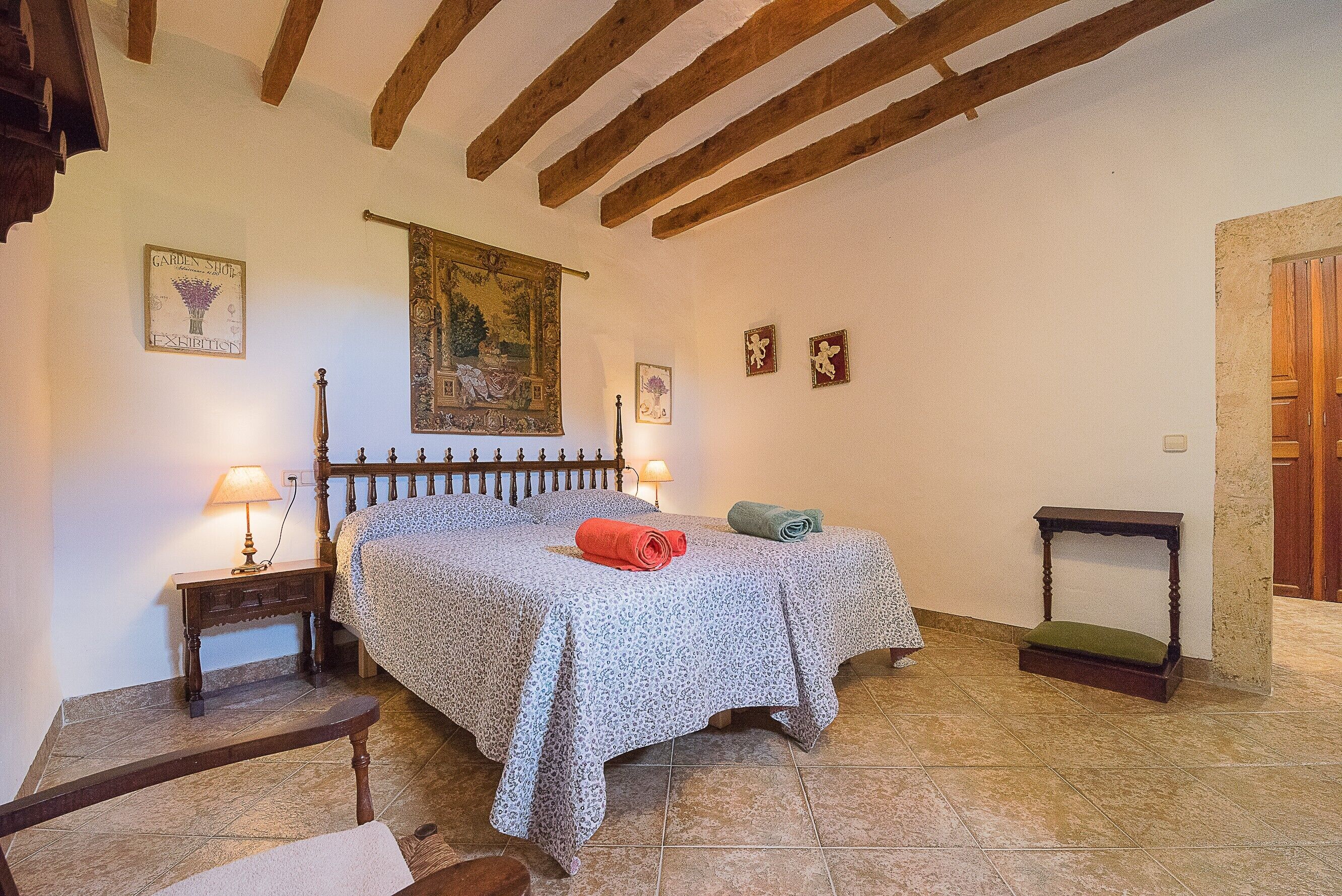 Un dormitorio con una cama, una mesita de noche, un banco y una pequeña mesa.