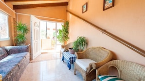 Un espacio interior acogedor con mobiliario de mimbre, una mesa con mantel a cuadros azul y blanco, y plantas en macetas.