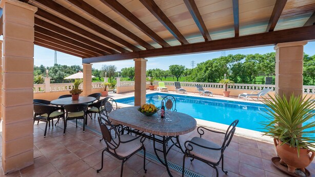 Un patio cubierto con piscina, mobiliario exterior y vistas del paisaje circundante.