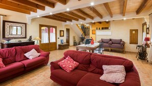 Ein geräumiges Wohnzimmer mit Holzbalken, roten Sofas, einer Treppe und einem Essbereich.
