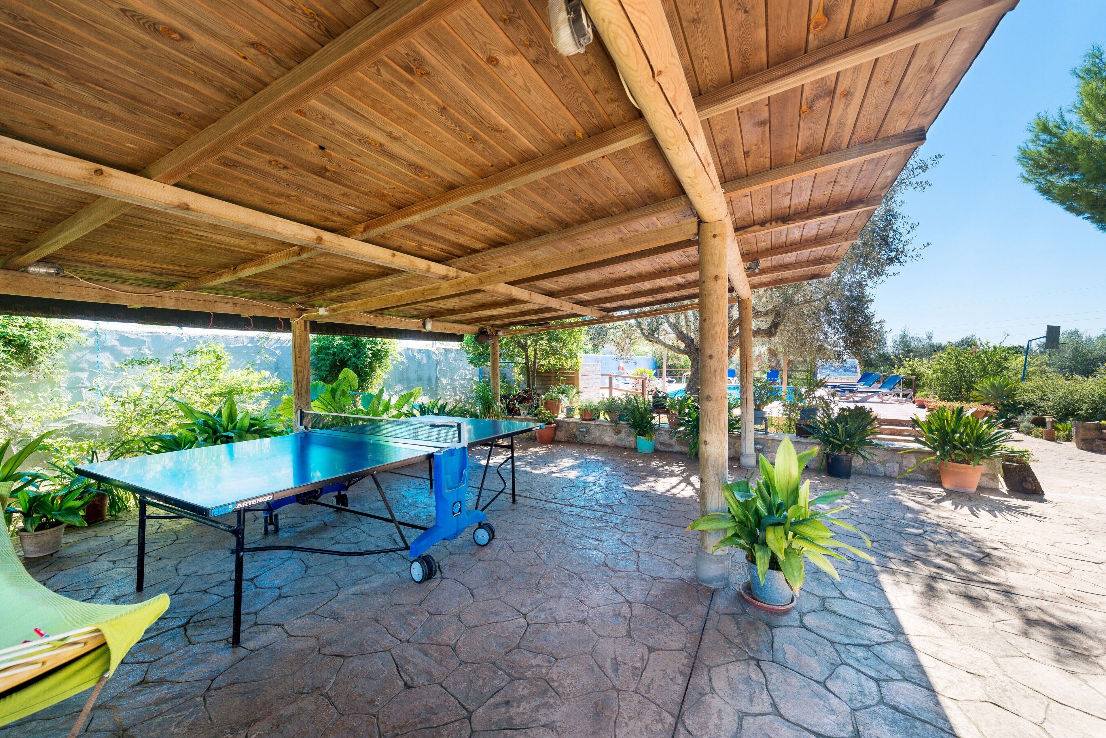 Un área de patio techada al aire libre con una mesa de ping pong, plantas en macetas y piso de piedra.