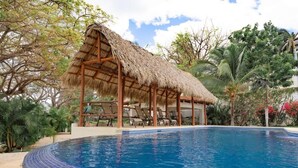A swimming pool with a thatched-roof pavilion and lounge chairs. - Oceanica 824- 2 Bedroom Ocean View Condo (Flamingo)