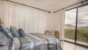 A bedroom with a large bed, a chair, and a balcony with a view of the countryside. - Oceanica 824- 2 Bedroom Ocean View Condo (Flamingo)