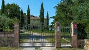 A gated entrance with a stone wall and a metal gate, leading to a building with a tiled roof. - Stunning private villa for 17 people with private pool, WIFI, TV, veranda and panoramic view (San Pancrazio)