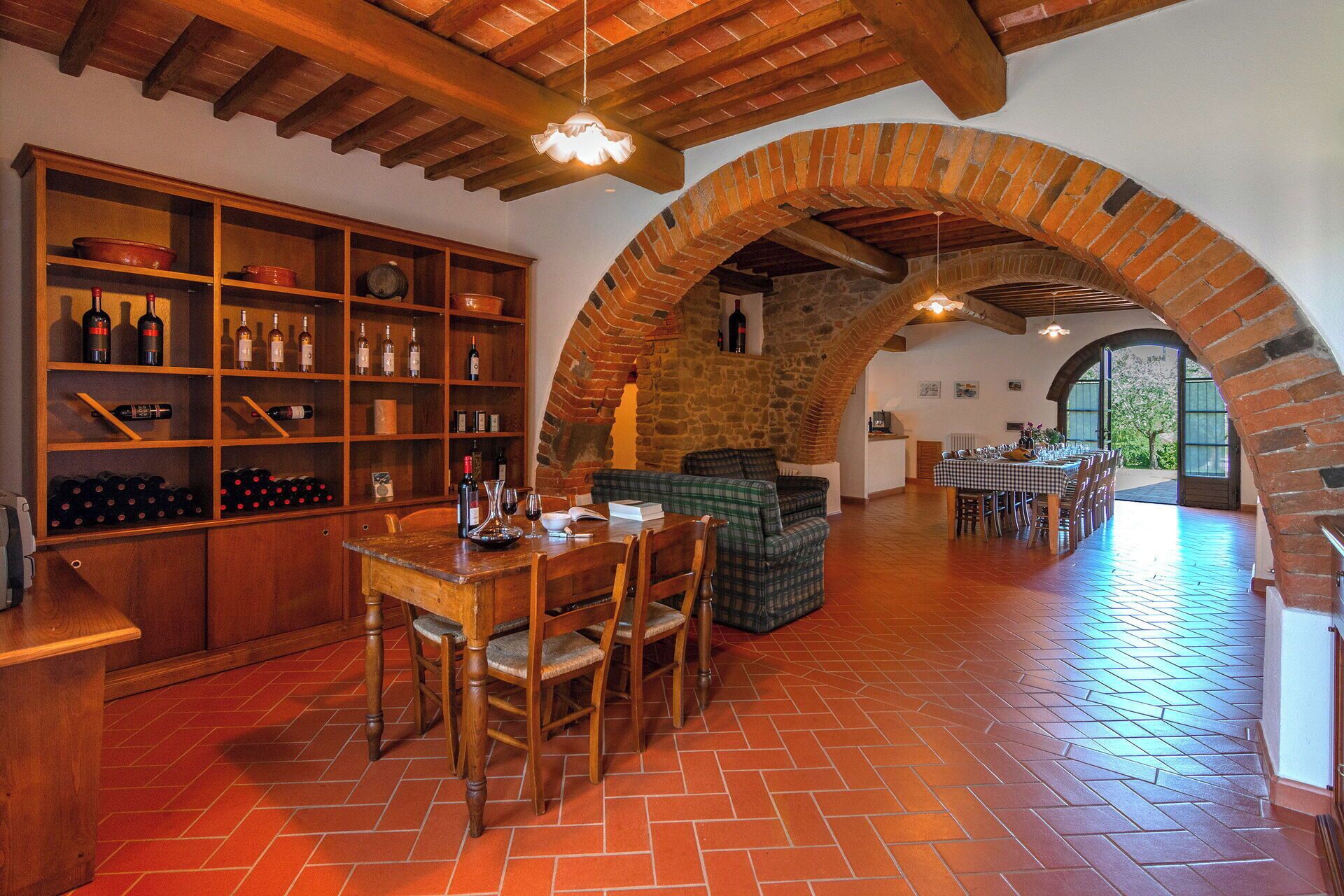 Un coin repas rustique agrémenté d’une arche en briques, de meubles en bois et d’un meuble à vin où sont exposées les bouteilles.
