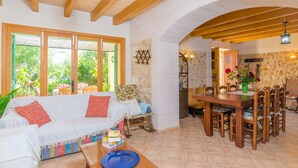 A cozy living room with a wooden ceiling, a dining area with a wooden table and chairs, and a stone wall with a decorative light fixture. - SA MATA - Spectacular Majorcan finca with private pool enclosed by the trees and greenery (Campanet)